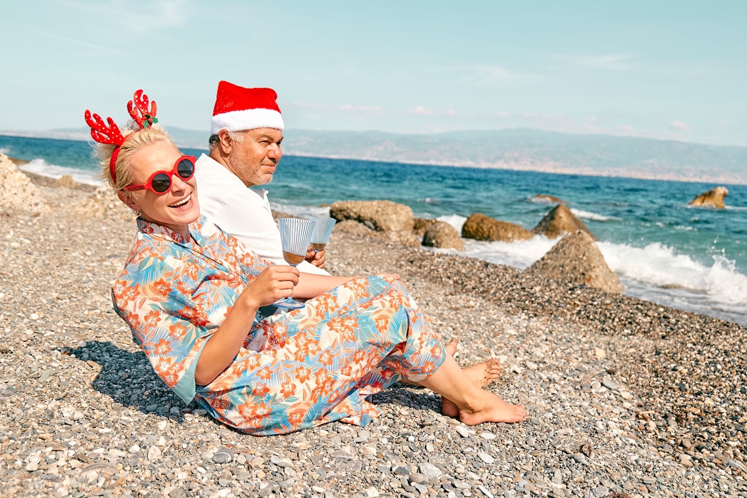 Funny adult couple wearing christmas costumes drinking sparkling wine and enjoying christmas vacations on tropical beach. Winter holiday concept. Monika Herbstrith-Lappe Humor nimmt den Druck