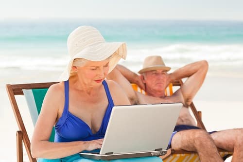 Woman working on her laptop while her husband is sleeping at the beach
